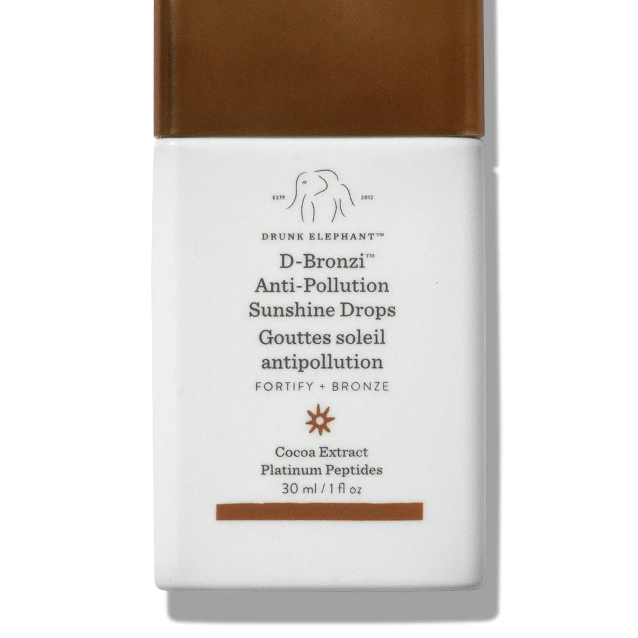 A rectangular shaped bottle of Drunk Elephant bronzing drops—a white bottle with brown cap against white background