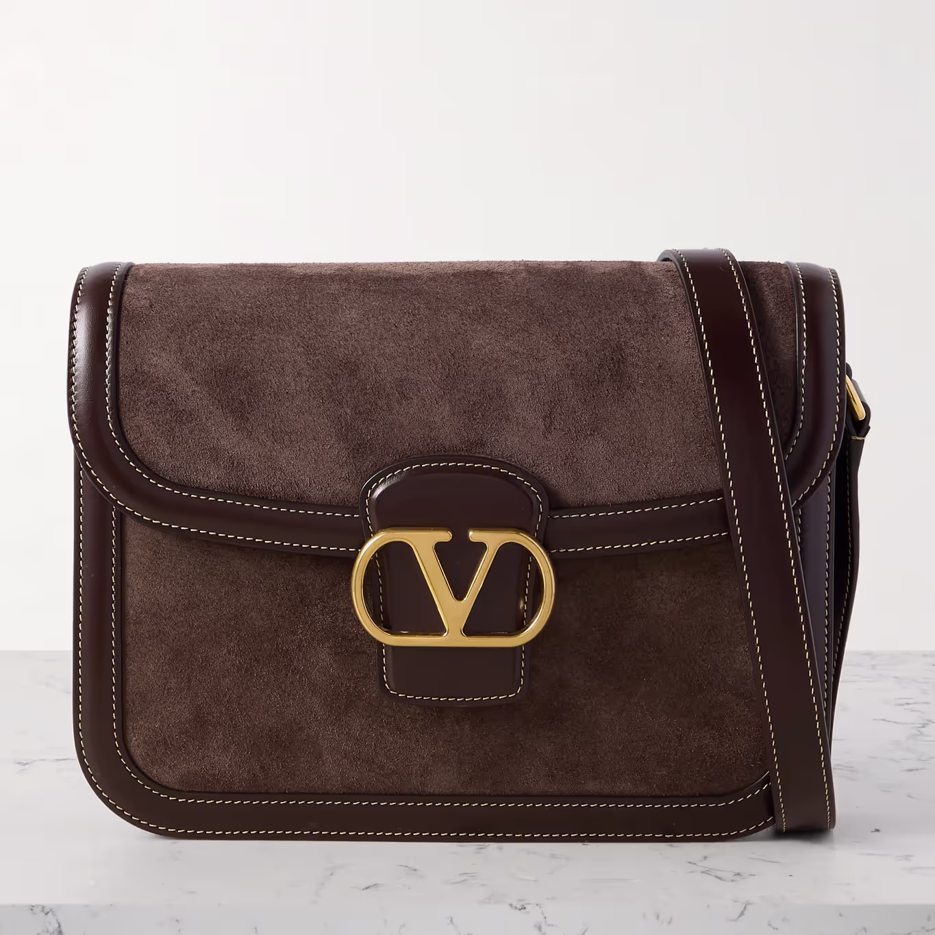The Valentino Garavani 9to5 leather-trimmed suede shoulder bag on a gray table