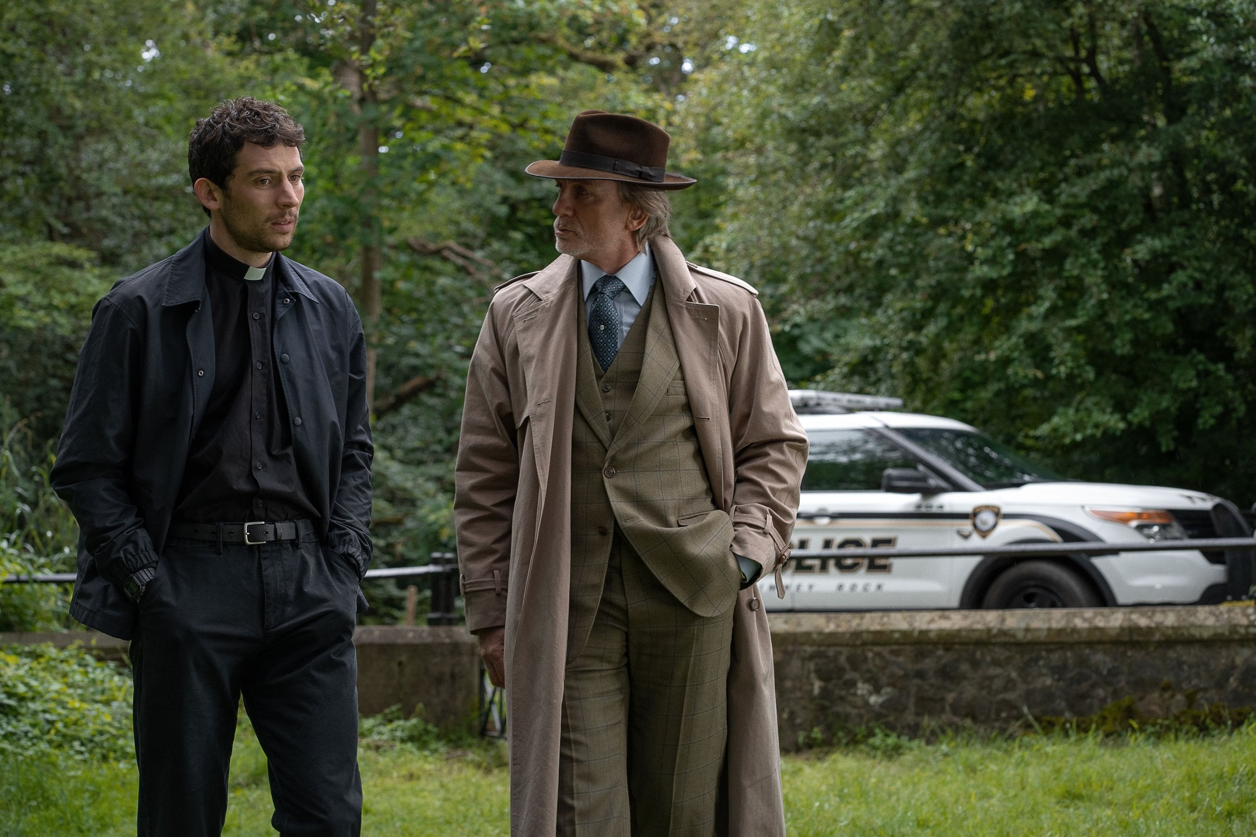 Actors Josh O'Connor and Daniel Craig stand around outside in a still from "Wake Up Dead Man: A Knives Out Mystery."