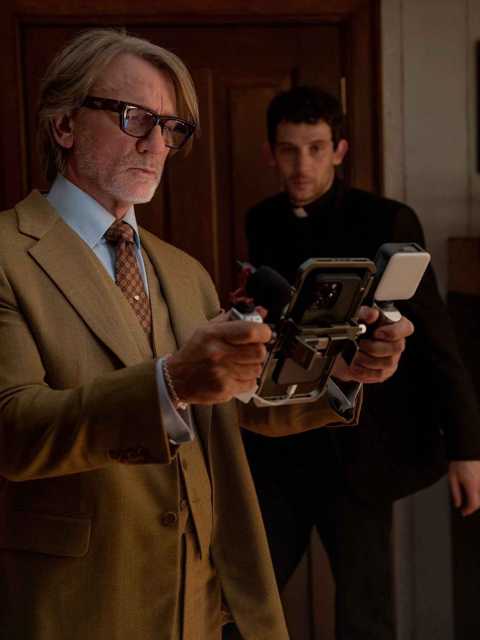 Actor Daniel Craig looks into an iPhone mounted on a large stand in a still from Wake Up Dead Man: A Knives Out Mystery.