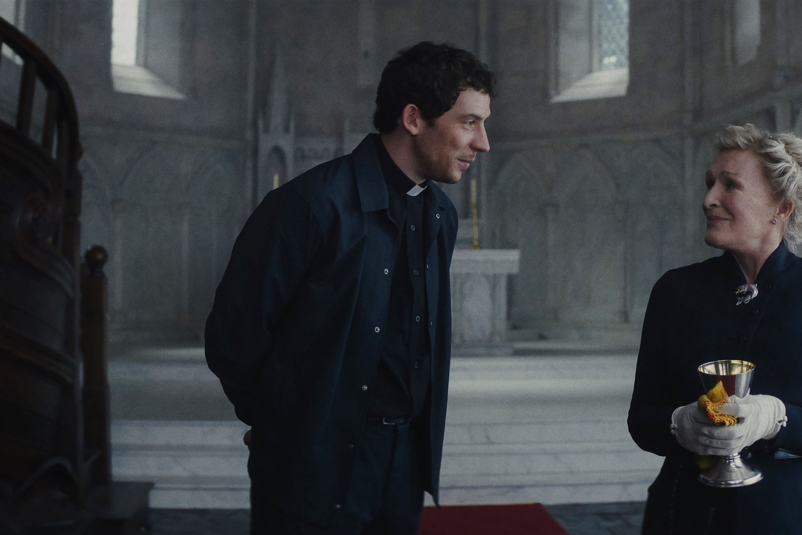 Actors Josh O'Connor and Glenn Close stand inside a church a still from "Wake Up Dead Man: A Knives Out Mystery."