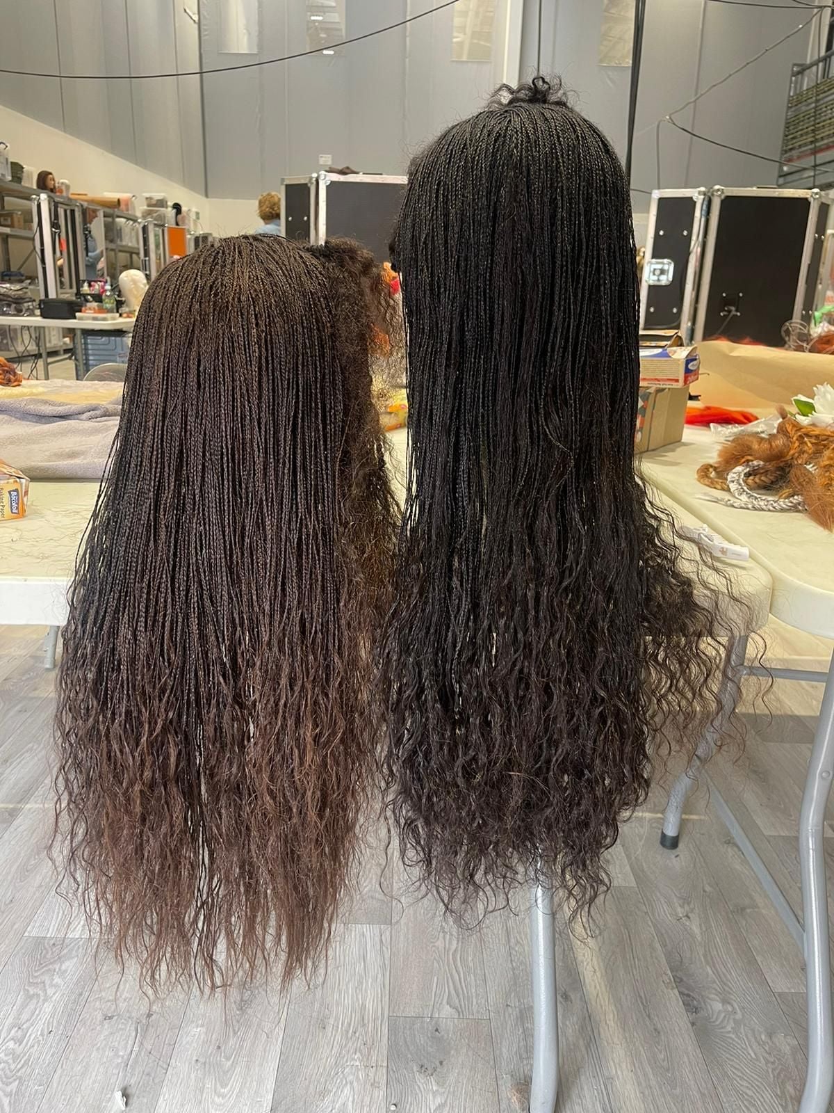 Two dark brown, micro-braided wigs hang on stands on set of Wicked: For Good.