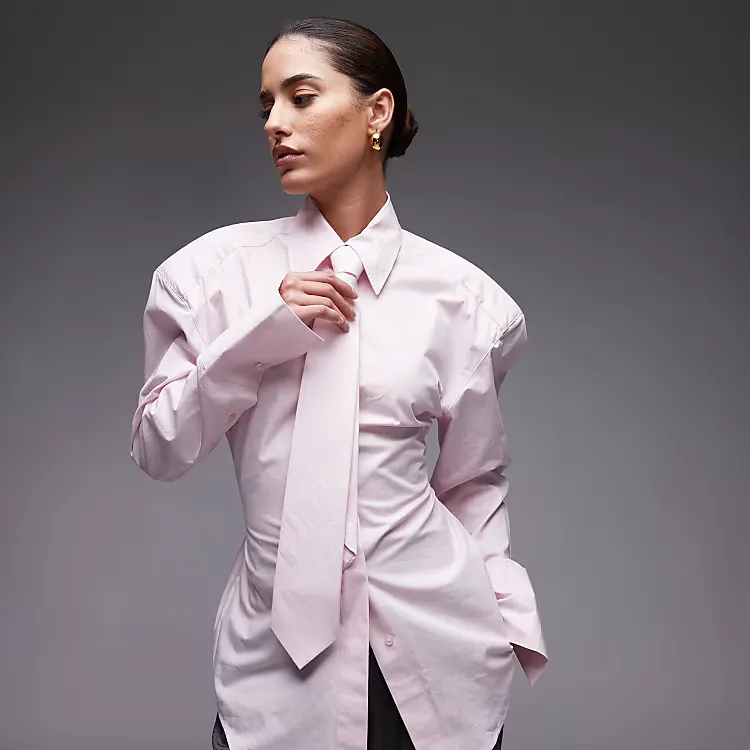 A model wears the ASOS Design cinch waist shirt with shoulder pads and necktie in pink