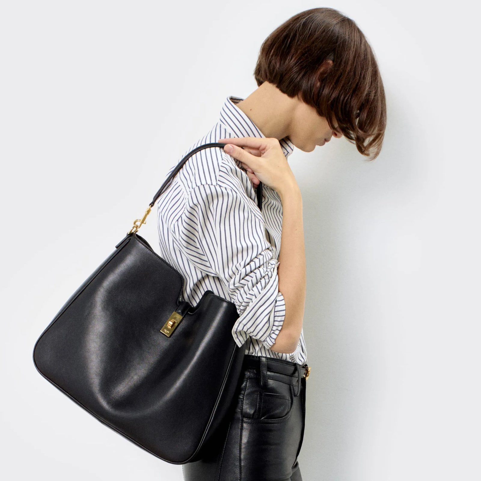 A model faces away from the camera, holding a black Celine Medium Camille 16 Soft Bag in Smooth Calfskin