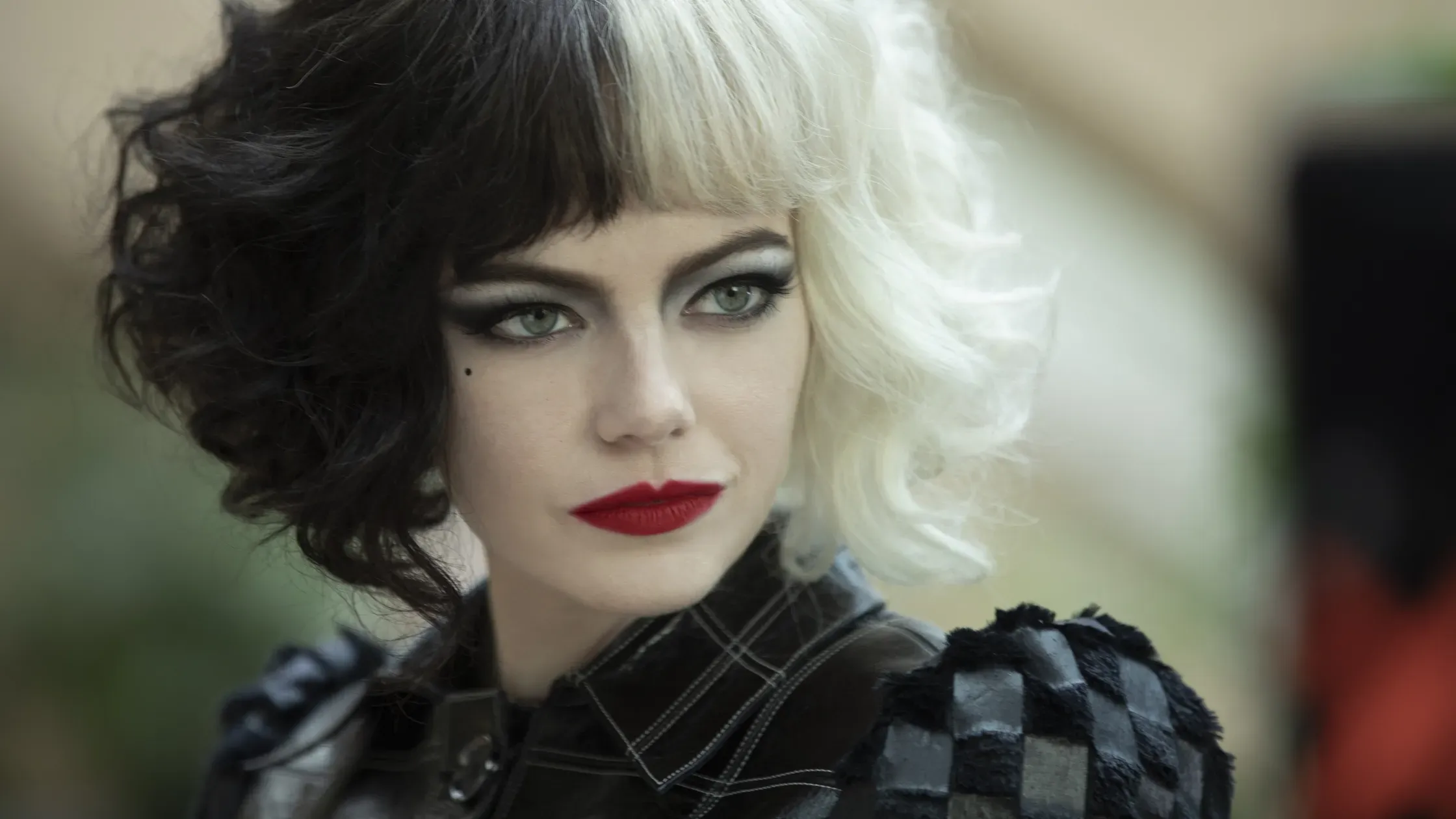 Emma Stone as Cruella in "Cruella," with a black-and-blonde wig, dark eyes, and red lipstick.