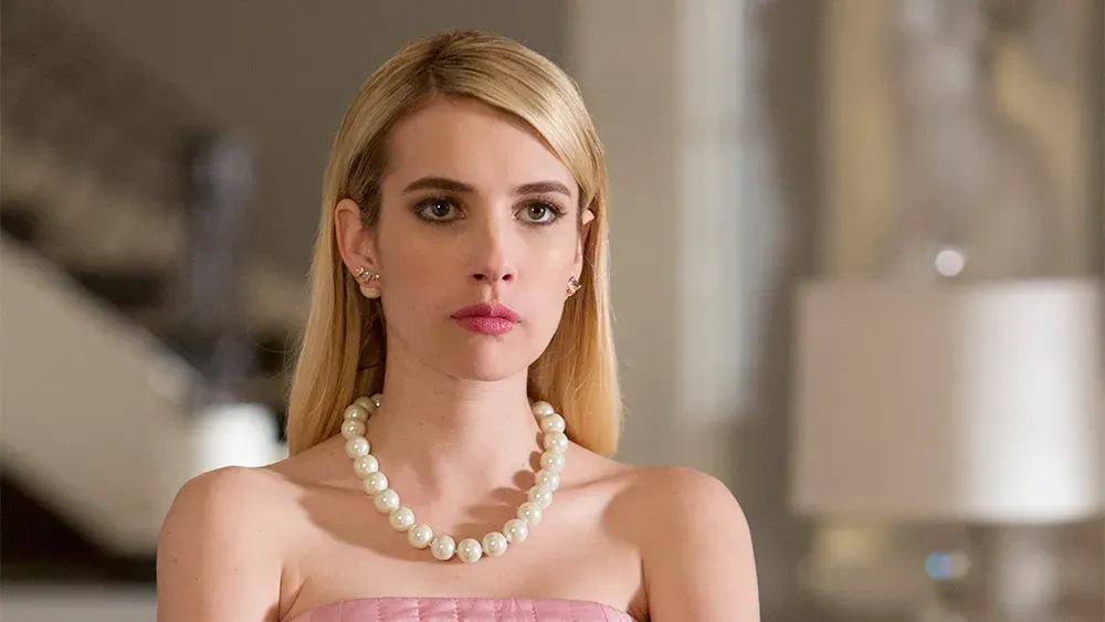 Emma Roberts in a pearl necklace and all pink in a scene from Scream Queens.