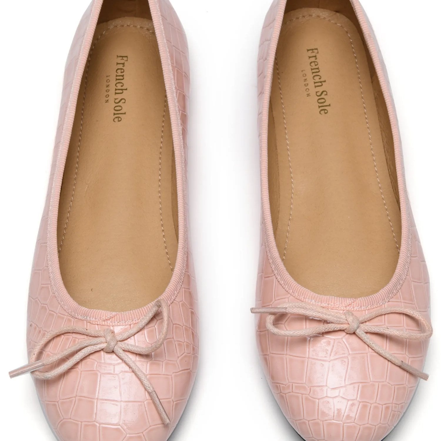 A pair of pink croc-textured ballet flats against a white background
