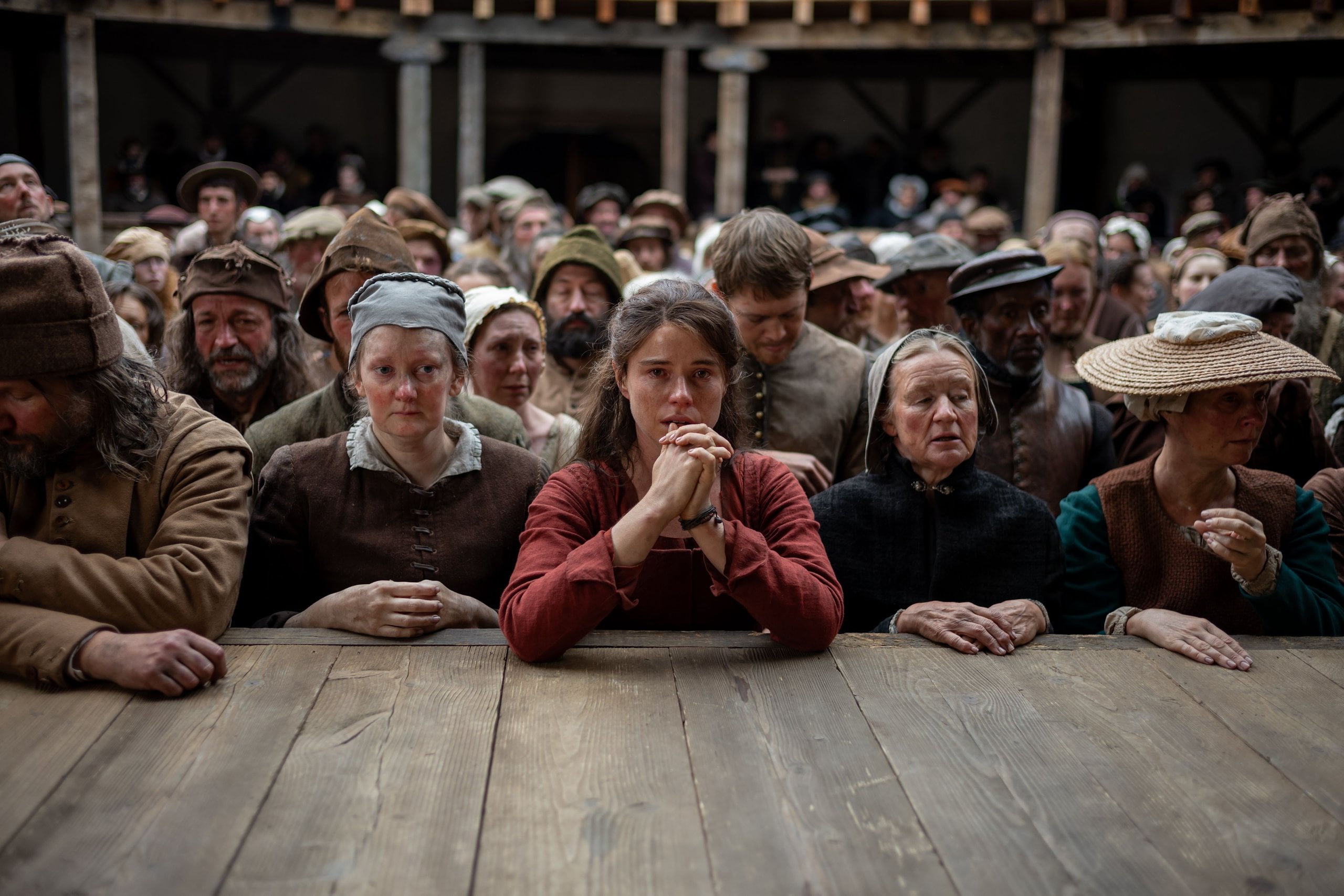 Actors Jessie Buckley and Joe Alwyn standing at the base of the stage of the Globe Theatre in a still from Hamnet.
