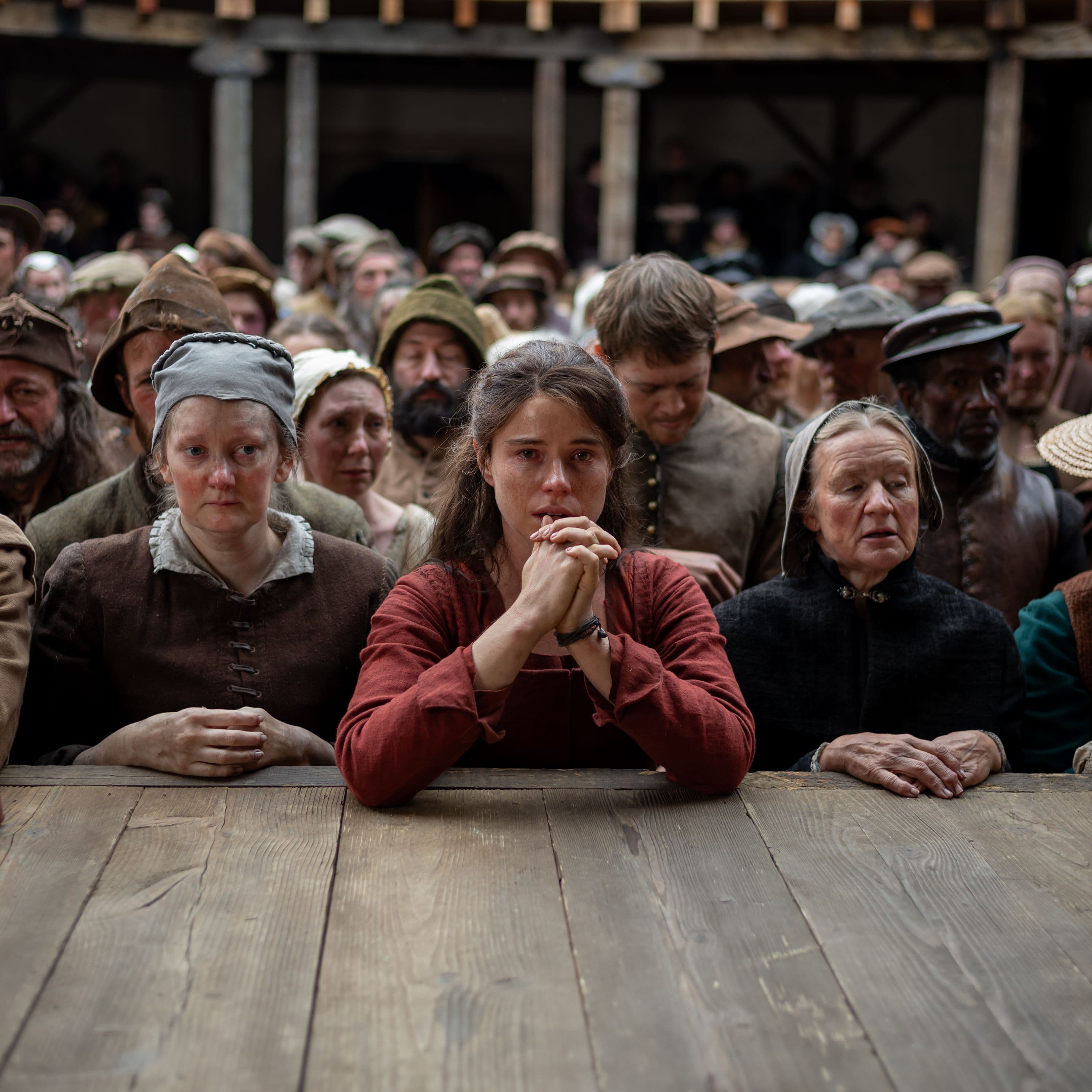 Actors Jessie Buckley and Joe Alwyn standing at the base of the stage of the Globe Theatre in a still from Hamnet.