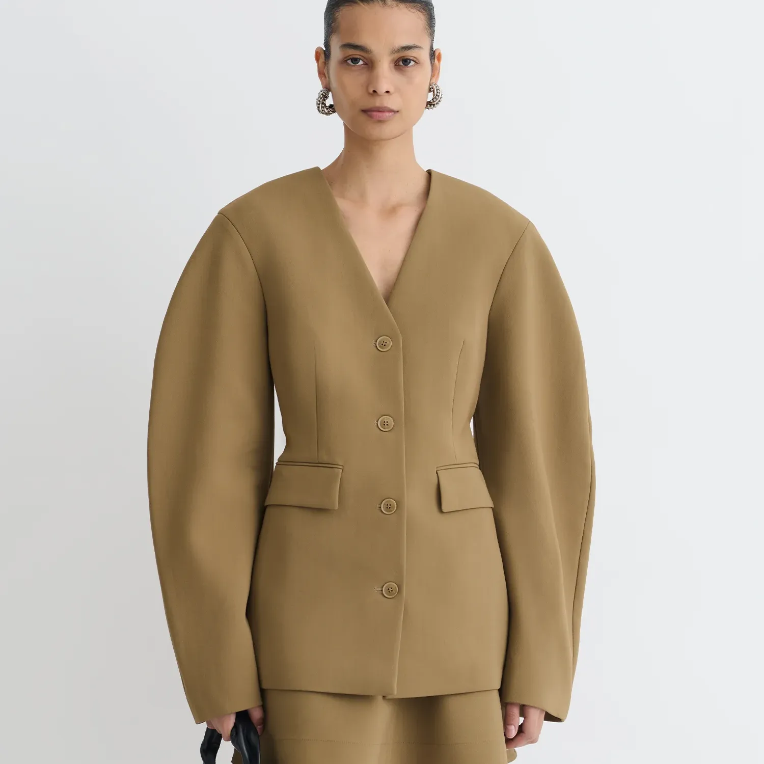 A model wears Nanushka Kaori Elongated Blazer in a camel color