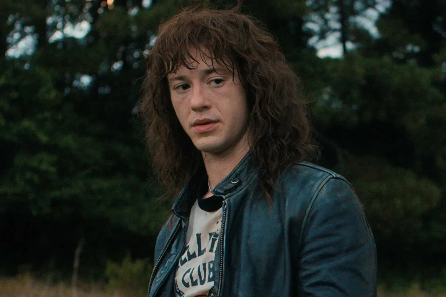 Actor Eddie Munson dressed in a leather jacket and a curly mullet in a still from Stranger Things.