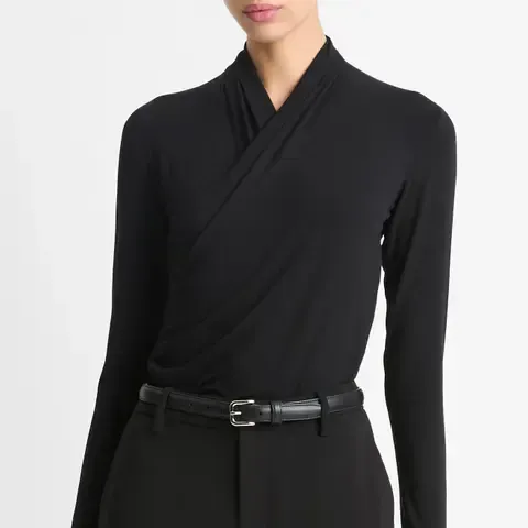 A model wears the a black Vince Long Sleeve Knit Wrap Top, black trousers, and black belt
